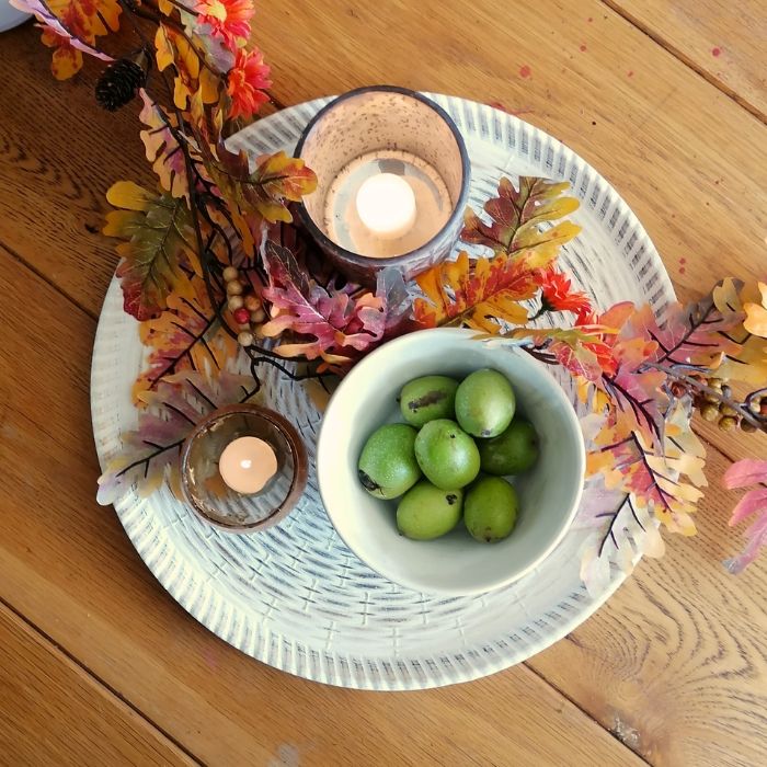 Flat lay of the large off white resin wicker-effect serving platter with bowl of green walnuts, and 2 candle holders with lit tea lights
