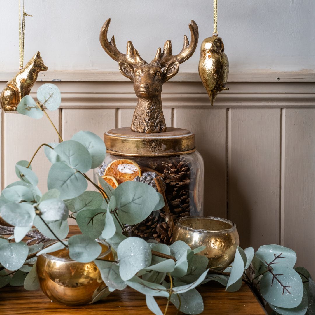 Decorative setup with gold deer head, candles, and eucalyptus leaves on a wooden surface.