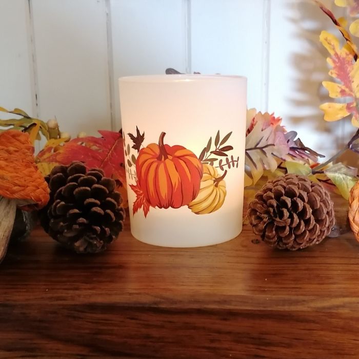 Decorative candle with pumpkins and leaves on a wooden surface with fall-themed decor.