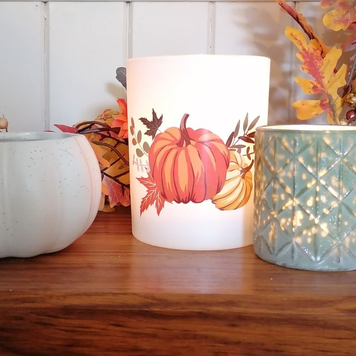 Decorative candle with pumpkin design on a wooden surface with autumn-themed decor.
