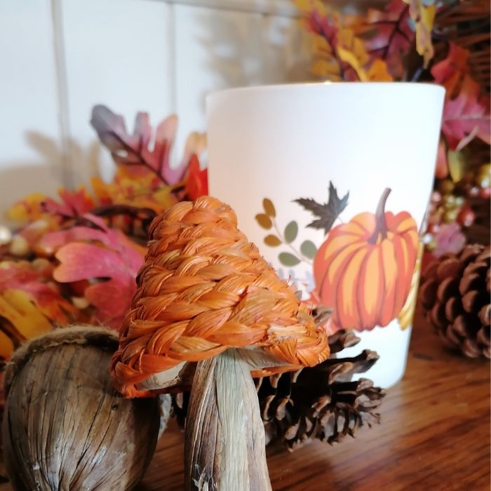 Decorative candle with autumn-themed design featuring pumpkins, leaves, and pinecones.