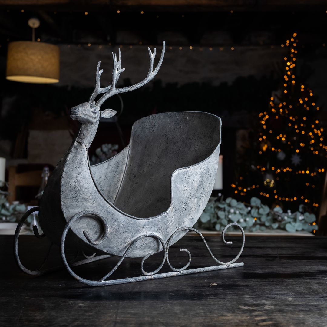 Decorative metal reindeer with sleigh on a dark surface, Christmas tree in the background