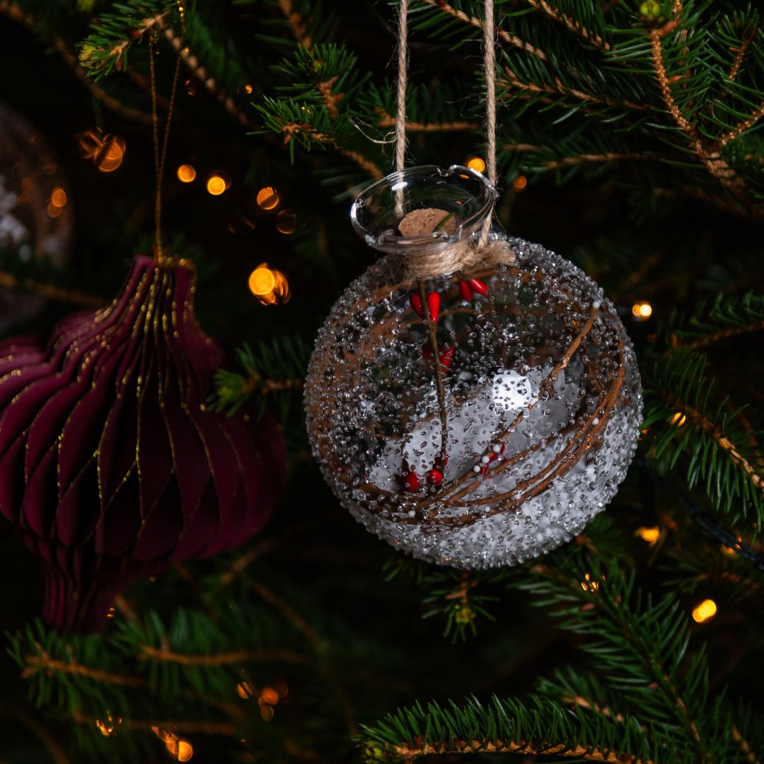 Decorative glass ornament with red berries hanging on a Christmas tree.