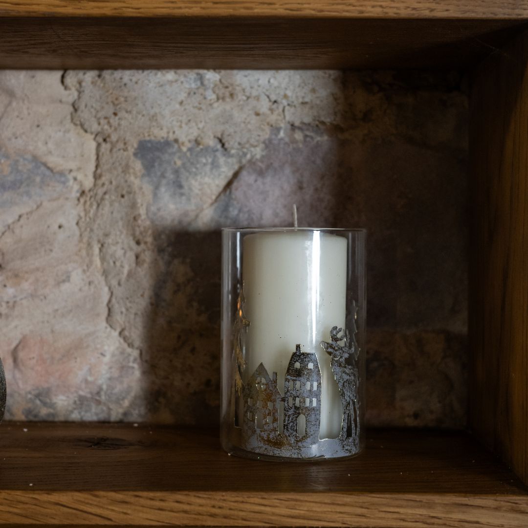 Candle with a decorative design of a winter scene on a wooden shelf against a stone wall.