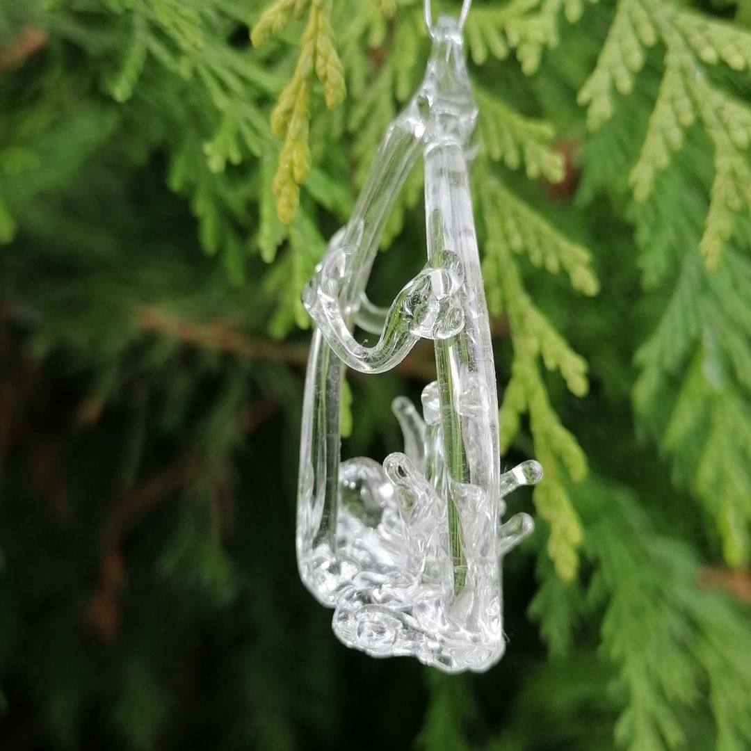 Clear glass ornament shaped side view of nativity hanging on green foliage