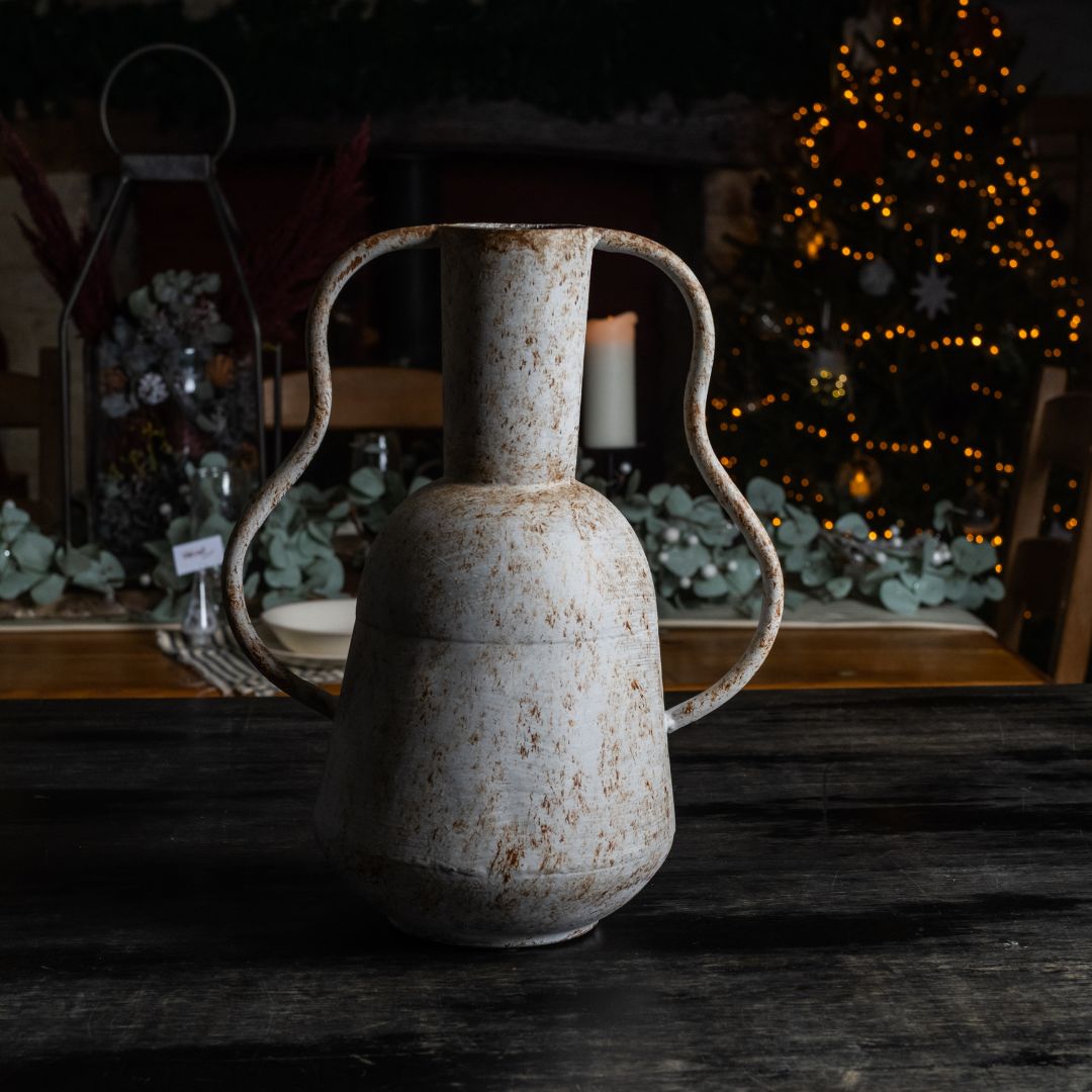 Vintage-style metal vase on a wooden surface with a softly blurred background