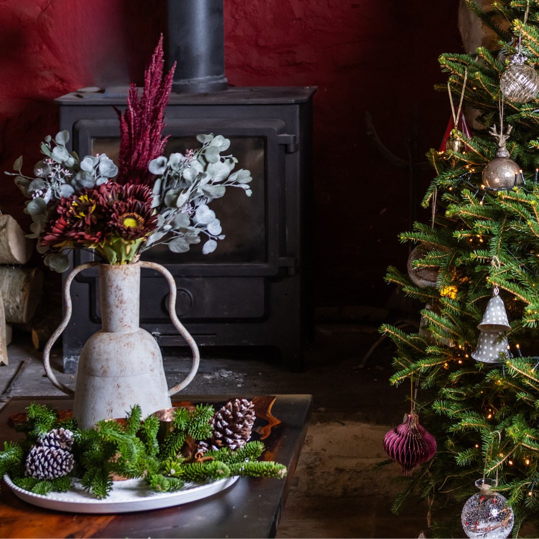Decorative setup with a Christmas tree, vase with flowers, and fireplace.