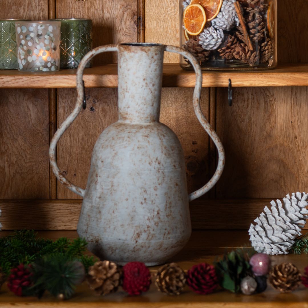 Decorative vase with handles on a wooden shelf with festive decorations.