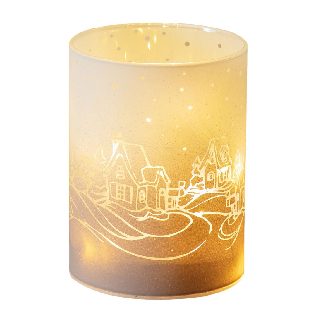 Cylindrical holder with a village design etched into it, emitting a warm glow.