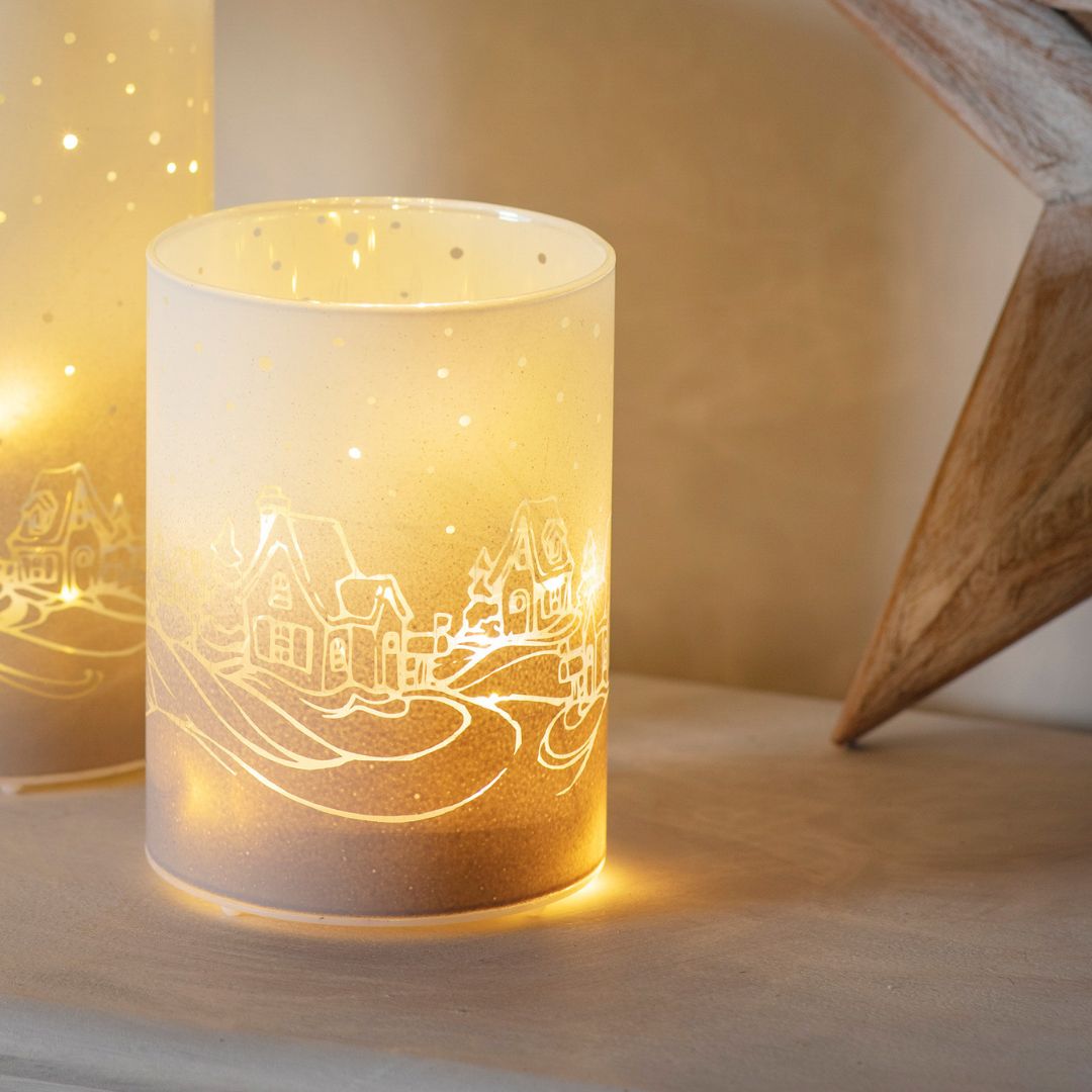 Decorative holder with a village design on a wooden surface glowing