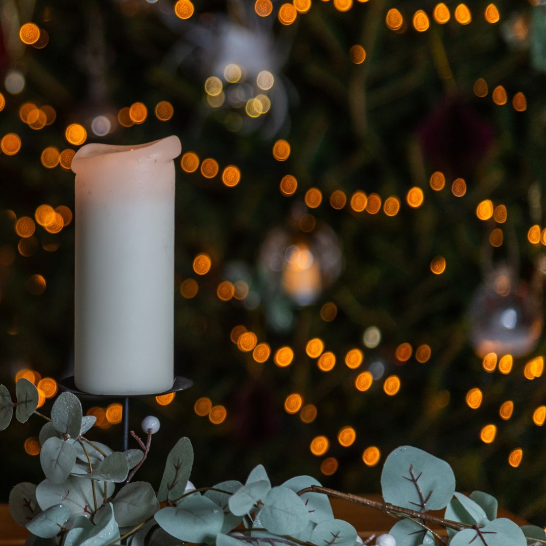 White candle on a eucalyptus holder with blurred tree lights in the background