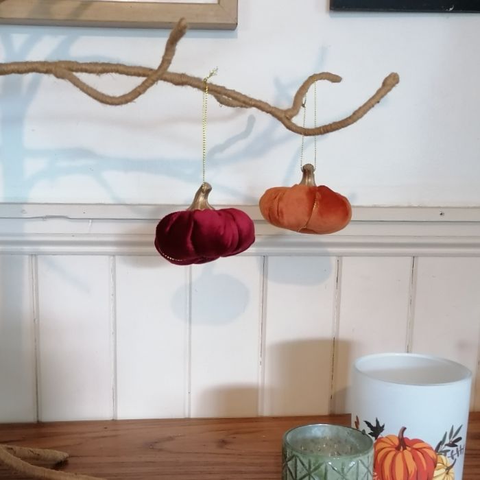 Decorative pumpkins hanging from a branch with a candle holder in the foreground.