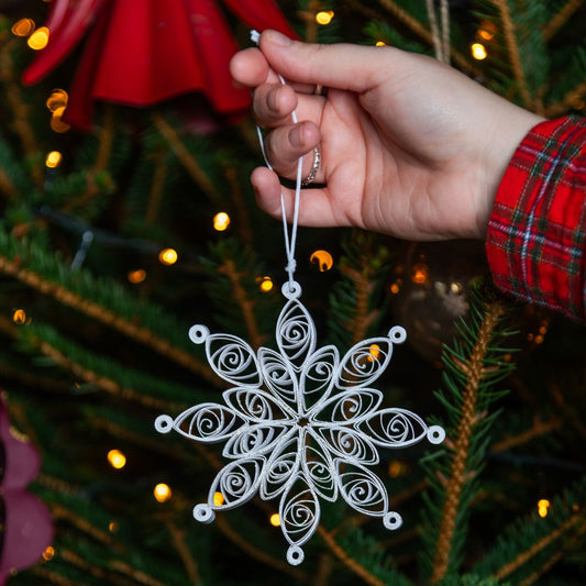 Hand holding a white snowflake ornament against a Christmas tree background