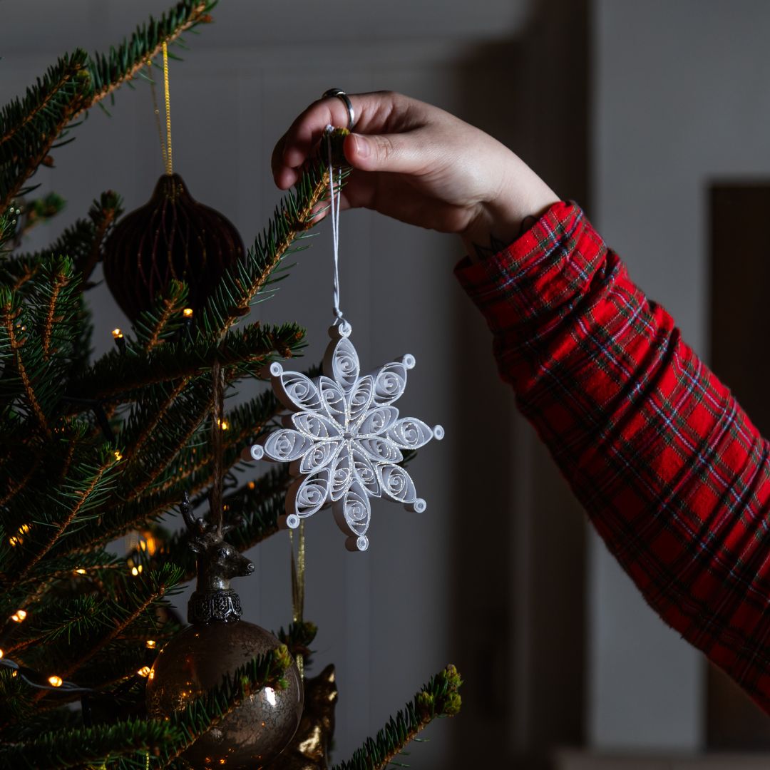 Person decorating a Christmas tree with a white snowflake ornament.