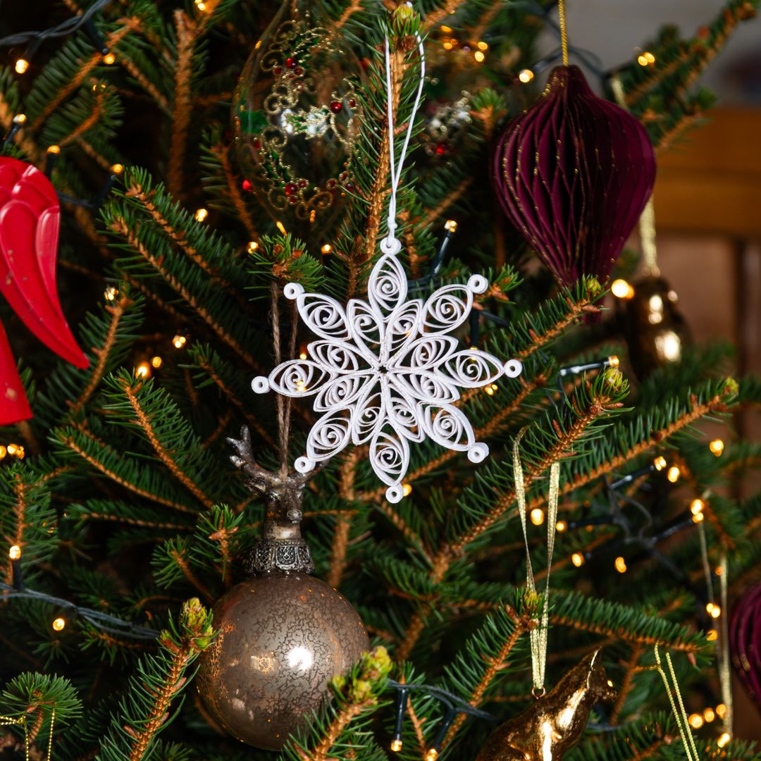 Decorative snowflake ornament hanging on a Christmas tree with other ornaments.