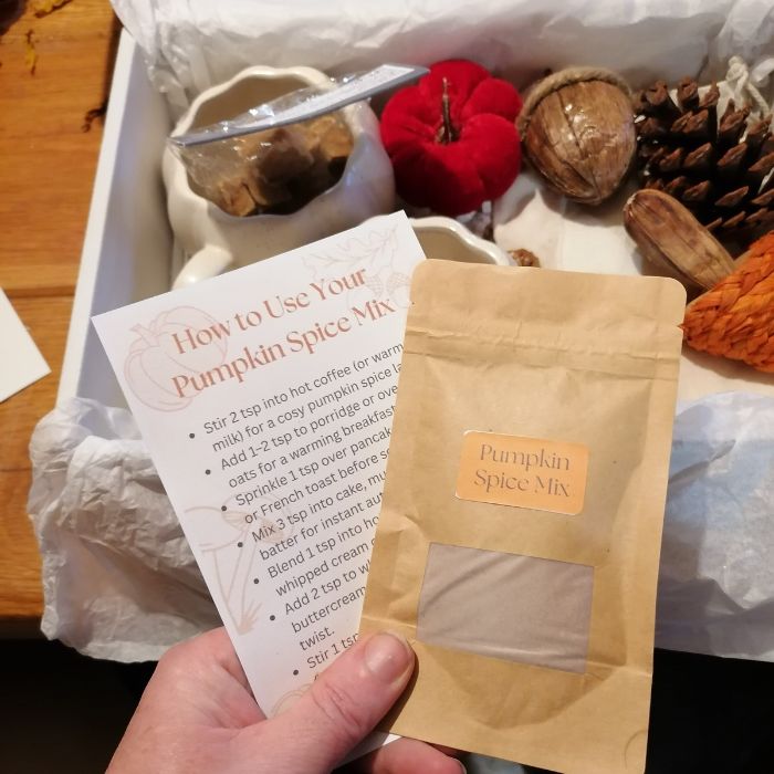 Pumpkin spice mix package with usage instructions held by a hand, surrounded by decorative items.