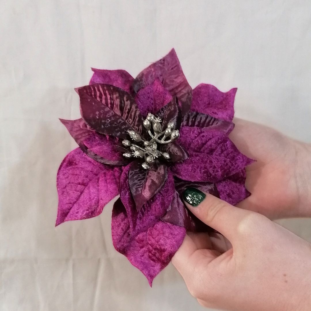Showing the purple silk poinsettia decoration in a model's hands against a beige background