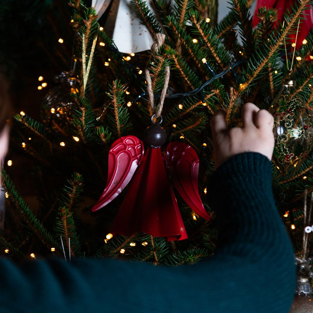 Person decorating a Christmas tree with a red angel ornament.