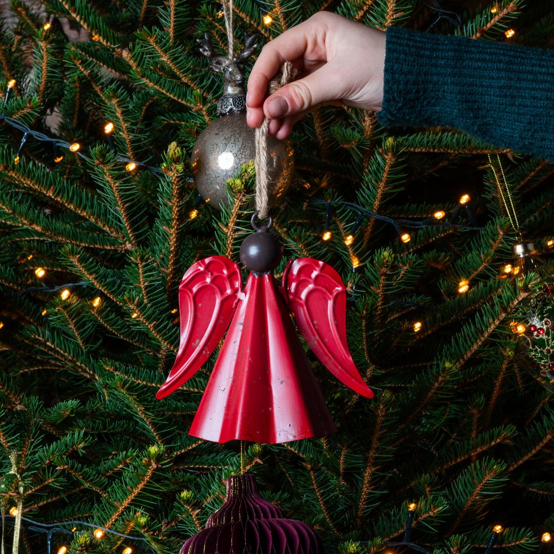 Hand holding a red angel wing ornament against a Christmas tree background