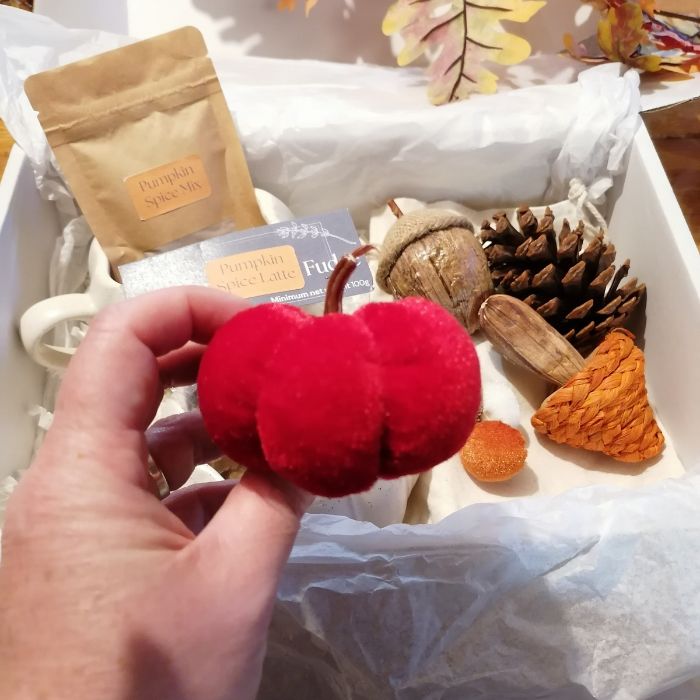 Red pumpkin-shaped toy held by a hand with a box of pumpkin spice latte and decorative items in the background.
