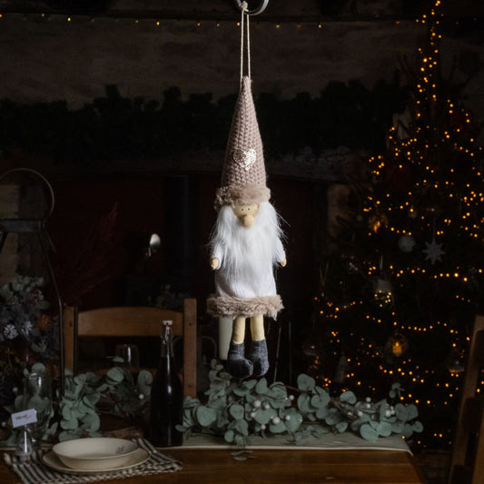 Knitted gnome hanging on a string with a blurred Christmas tree in the background