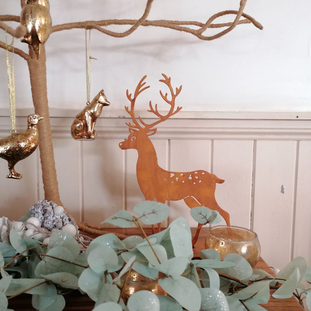 Rusty metal stag stading amongst green foliage next to a branch tree