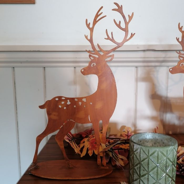 Decorative metal deer figure on a mantel with a candle and autumn leaves.