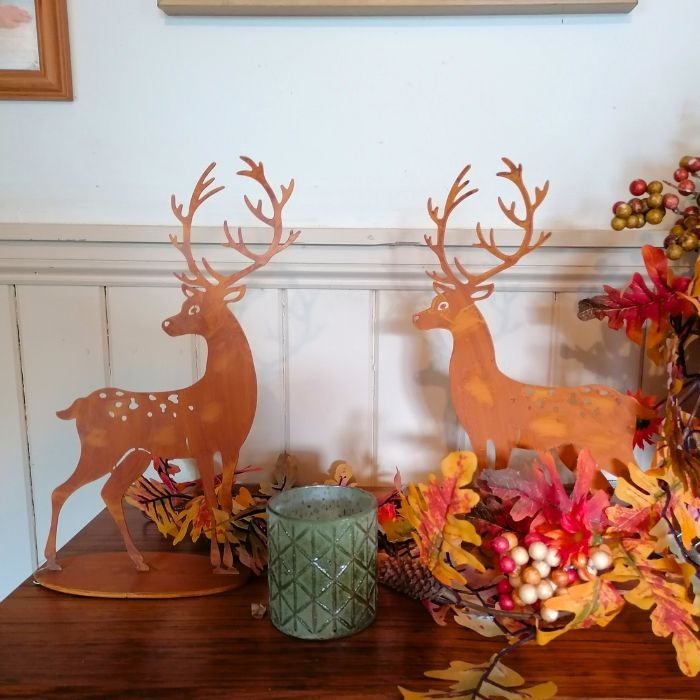 Two metal deer decorations on a wooden surface with fall-themed decor.