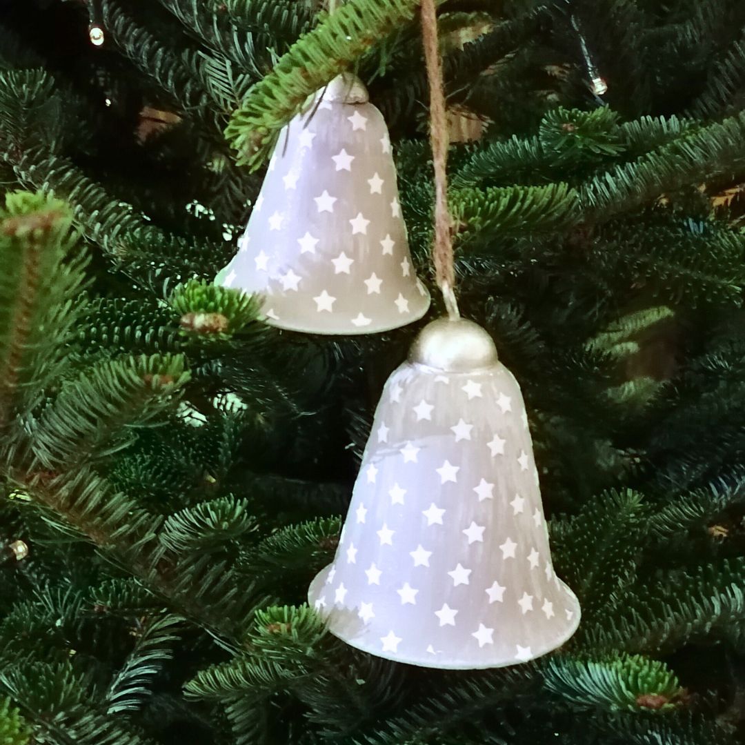 Two metal grey bells with stars hanging on a fir tree
