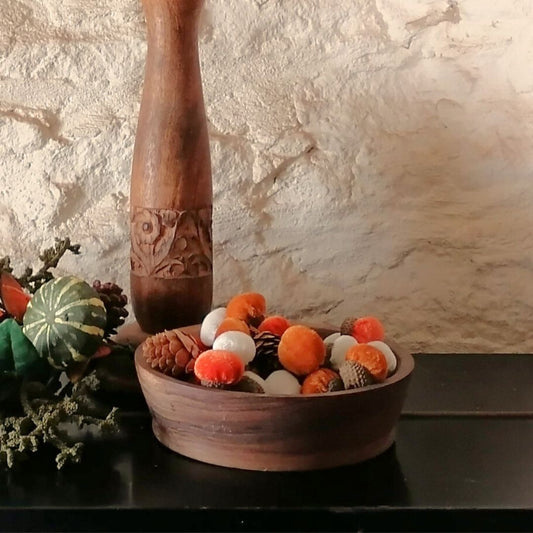 Velvet orange, white and burgundy acorns with rustic pinecones in a wooden bowl, with a curved candlestick in the background