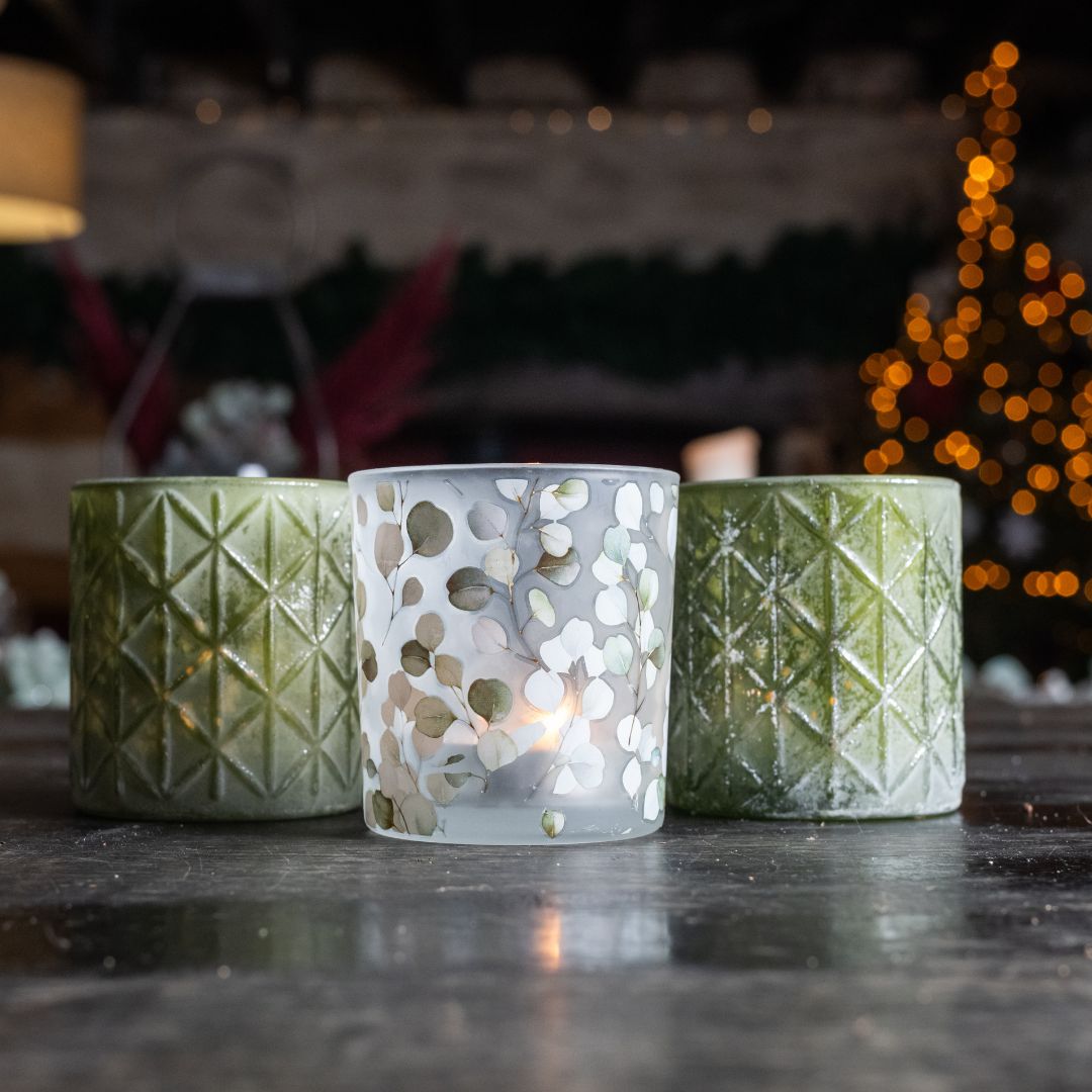 Three decorative candles with geometric patterns on a dark surface, blurred festive background.