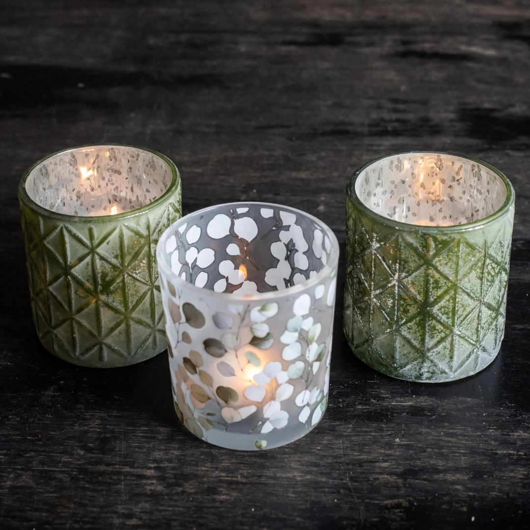Three patterned candle holders with lit candles on a dark wooden surface