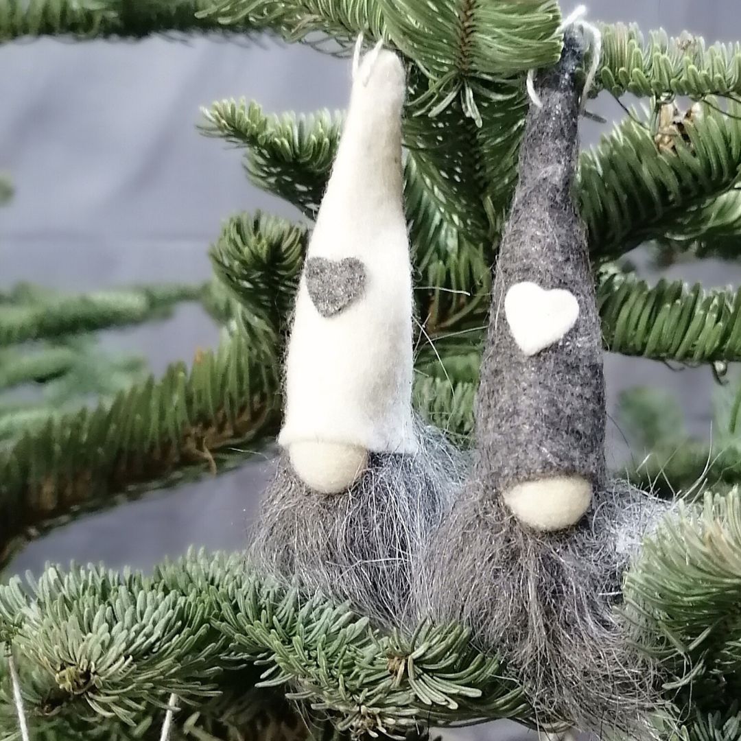 Showing a grey gonk and a white gonk decoration hanging in a Christmas tree, with a dark grey background