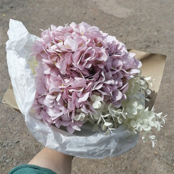 Bouquet of purple and white flowers wrapped in paper held by a person.