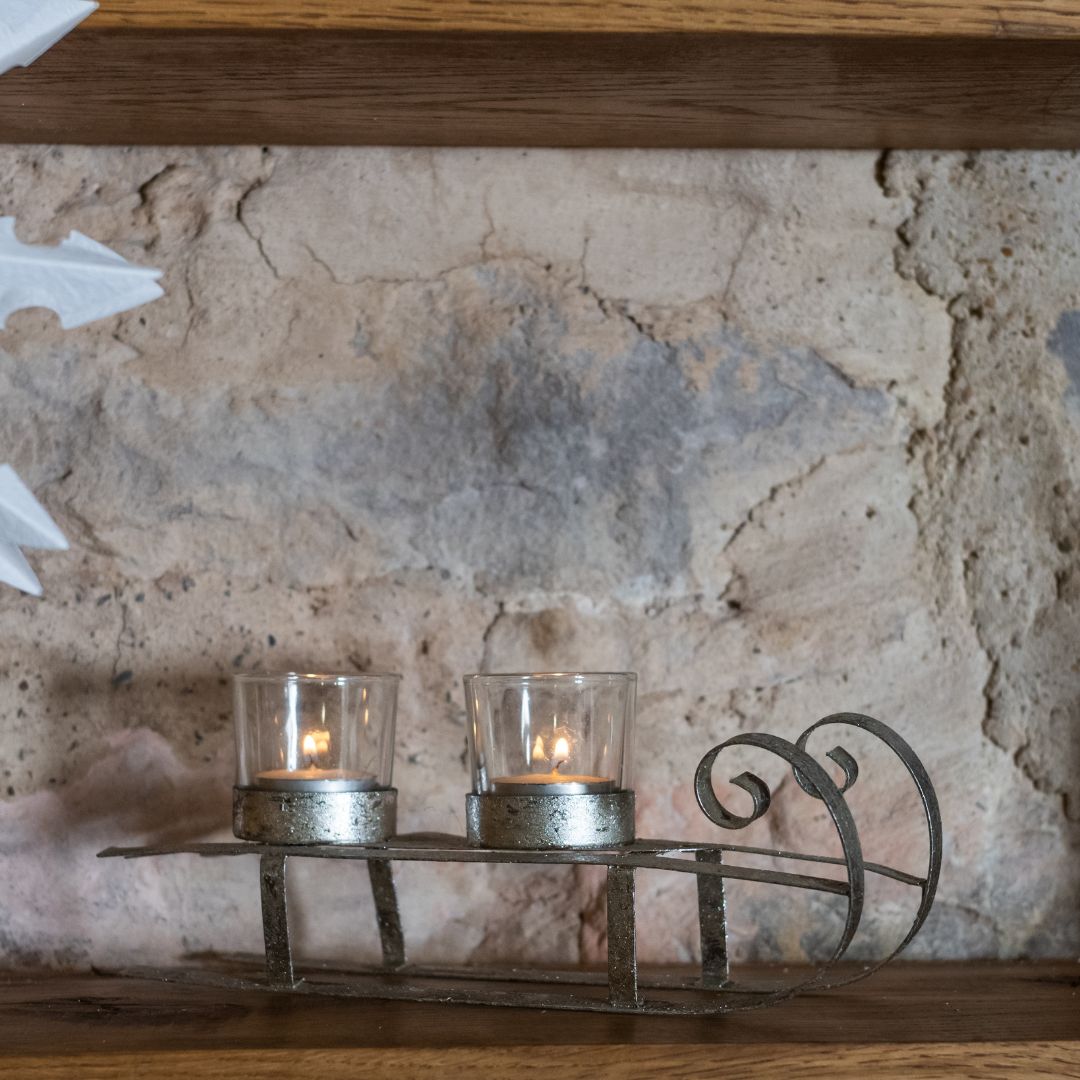 Decorative metal candle holder with two lit candles against a stone wall.