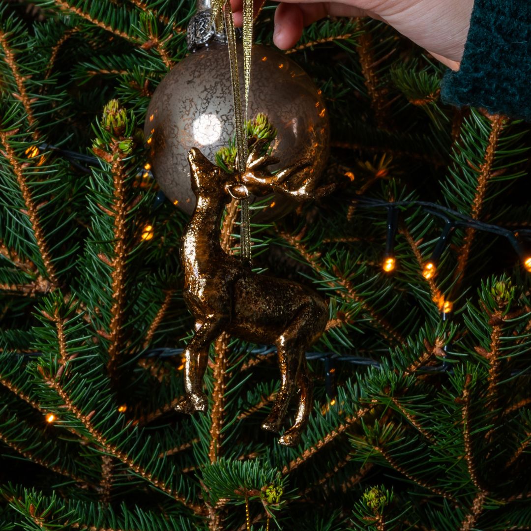 Gold deer ornament on a Christmas tree with a silver ball ornament.