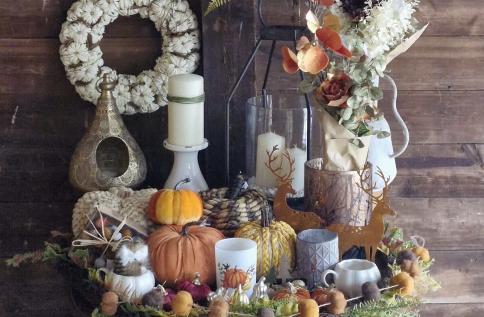 Autumn-themed decor with pumpkins, candles, and wreath on a wooden background