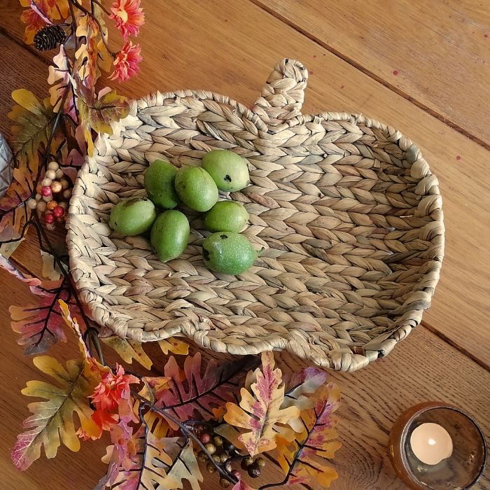 Woven basket with green walnuts on a wooden surface with autumn leaves and a candle.