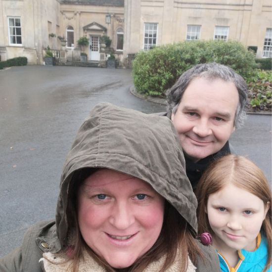 Two adults and a child standing in front of a large building with a driveway.
