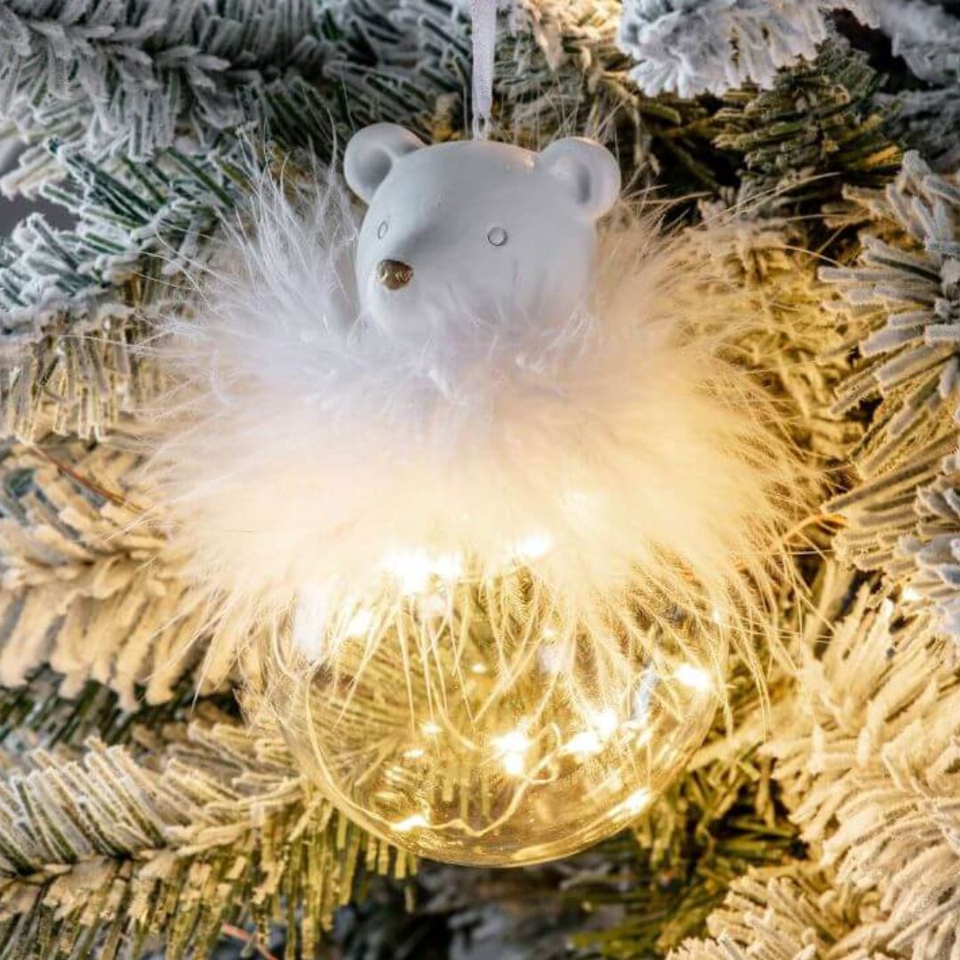 Picture of the white polar bear glass light up hanging decoration against a flocked Christmas tree background