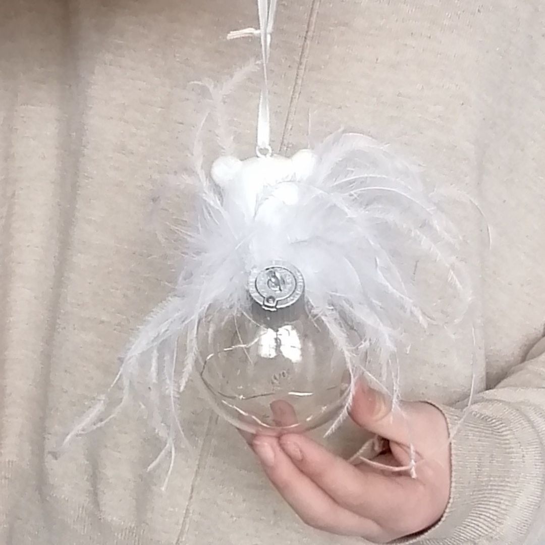 Image of the back of the white polar bear light up glass hanging decoration with the battery area against a beige jumper with a model's hands showing scale