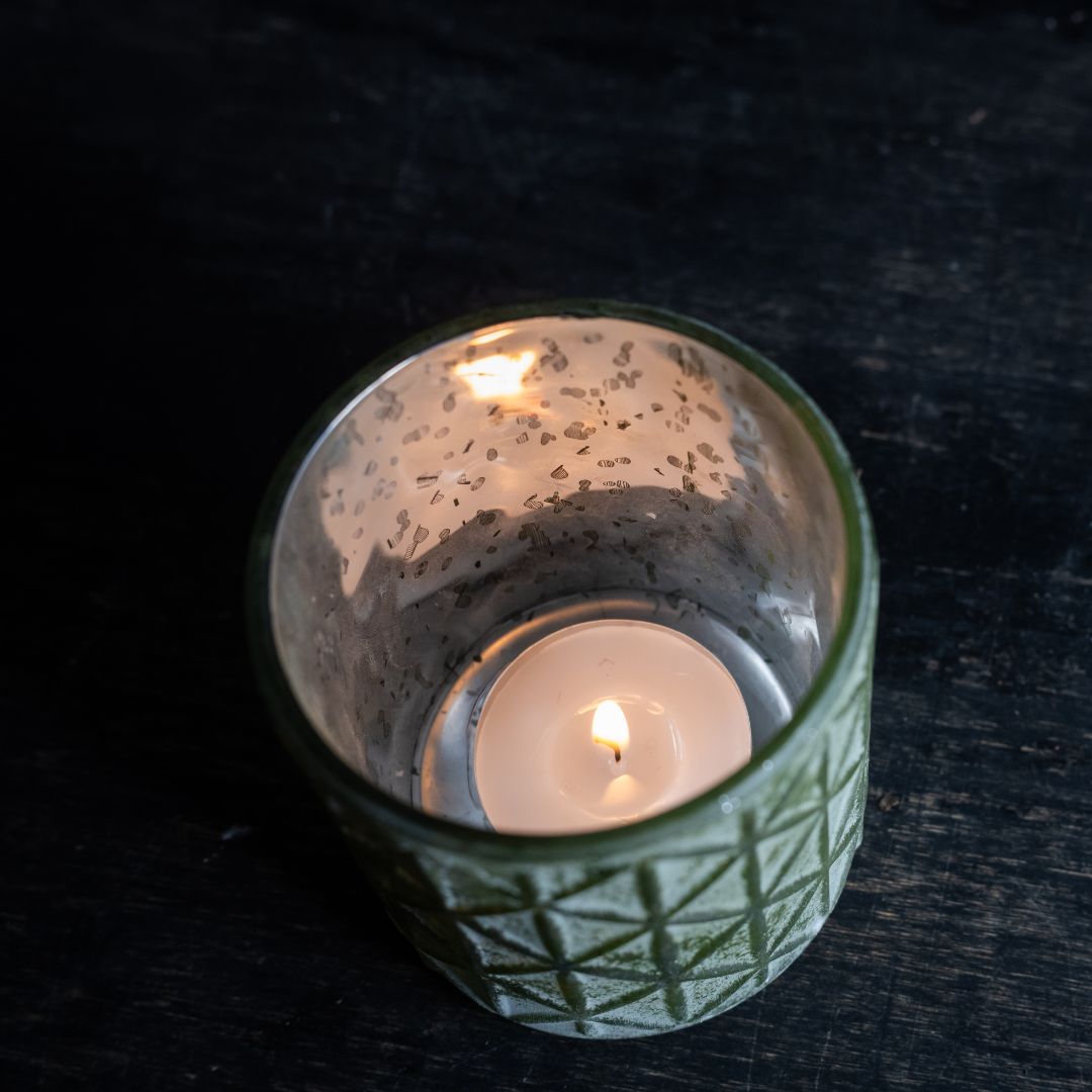 Glass candle holder with a lit candle on a dark surface