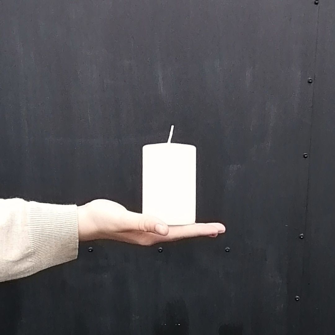 Short ivory fragrance-free wax pillar candle in model's hand to show scale against a black background