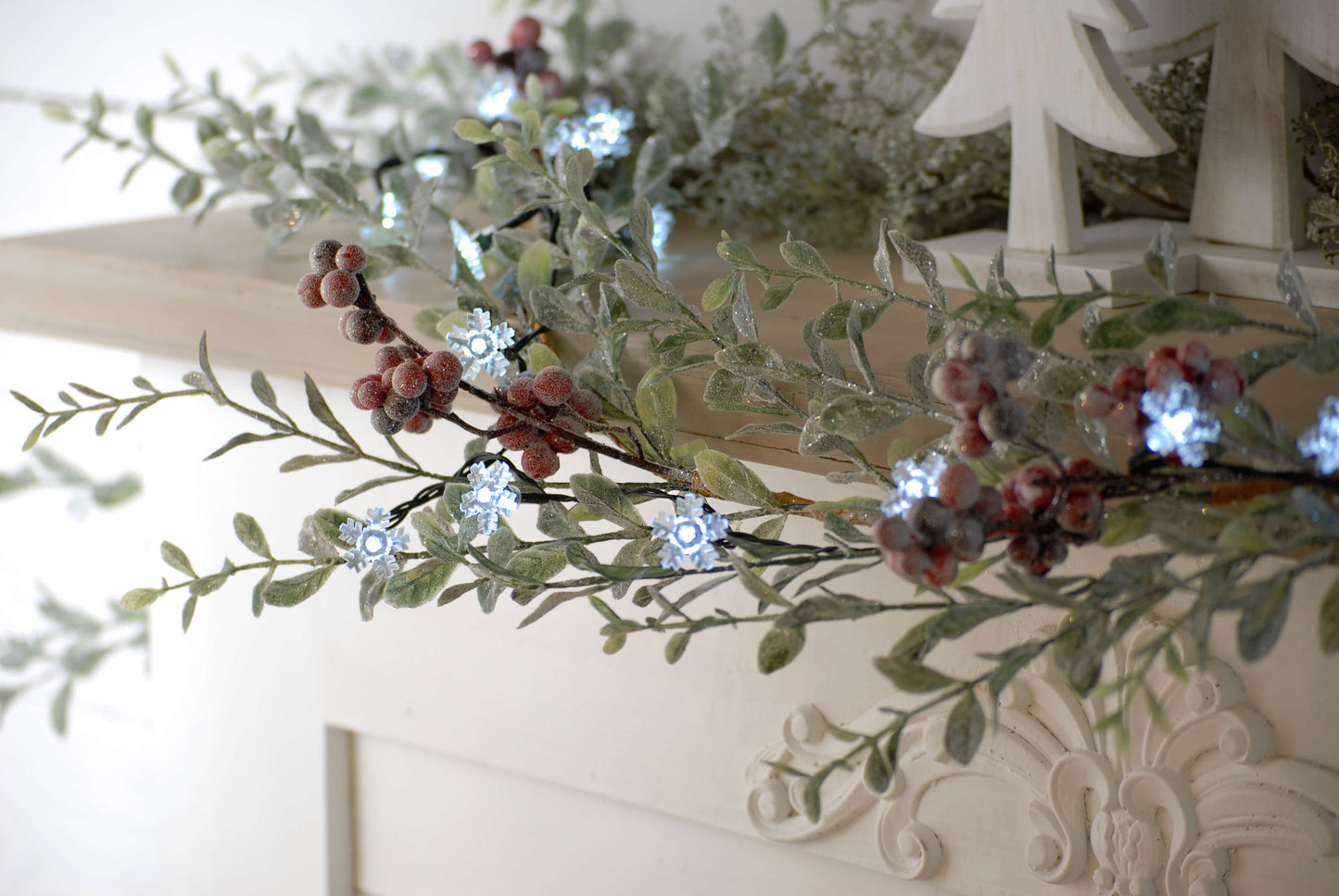 Battery snowflake Christmas lights decorating a Christmas garland on a mantelpiece