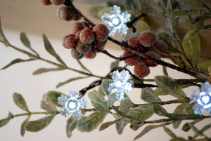 Close up of snowflake bulb next to berries on battery snowflake Christmas lights