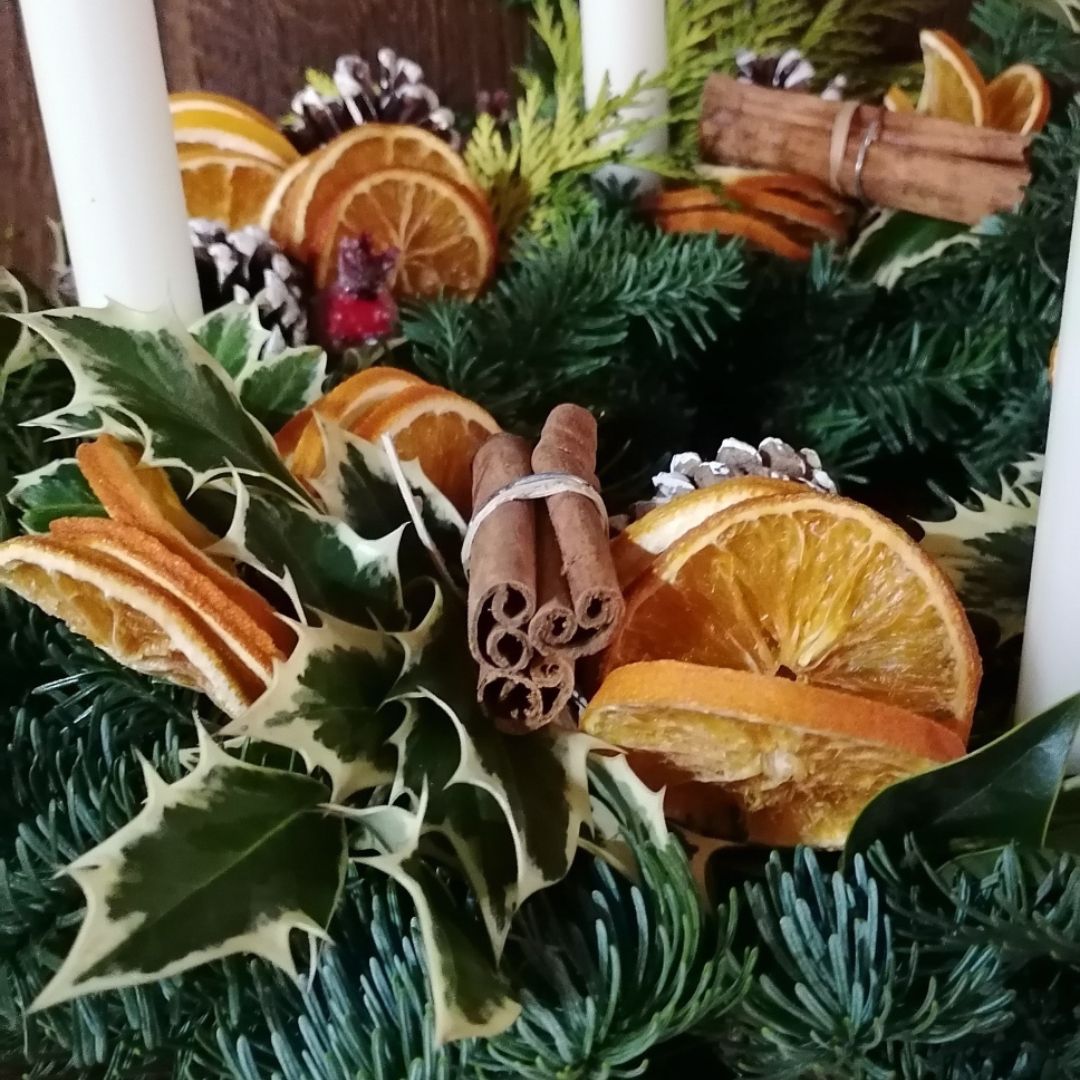 A close up of the fresh table centrepiece showing the orange slices, snow tipped fir cones, rosehip berries and cinnamon sticks