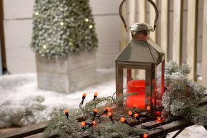 An image of the red berries Christmas lights on a garland next to a candle lantern