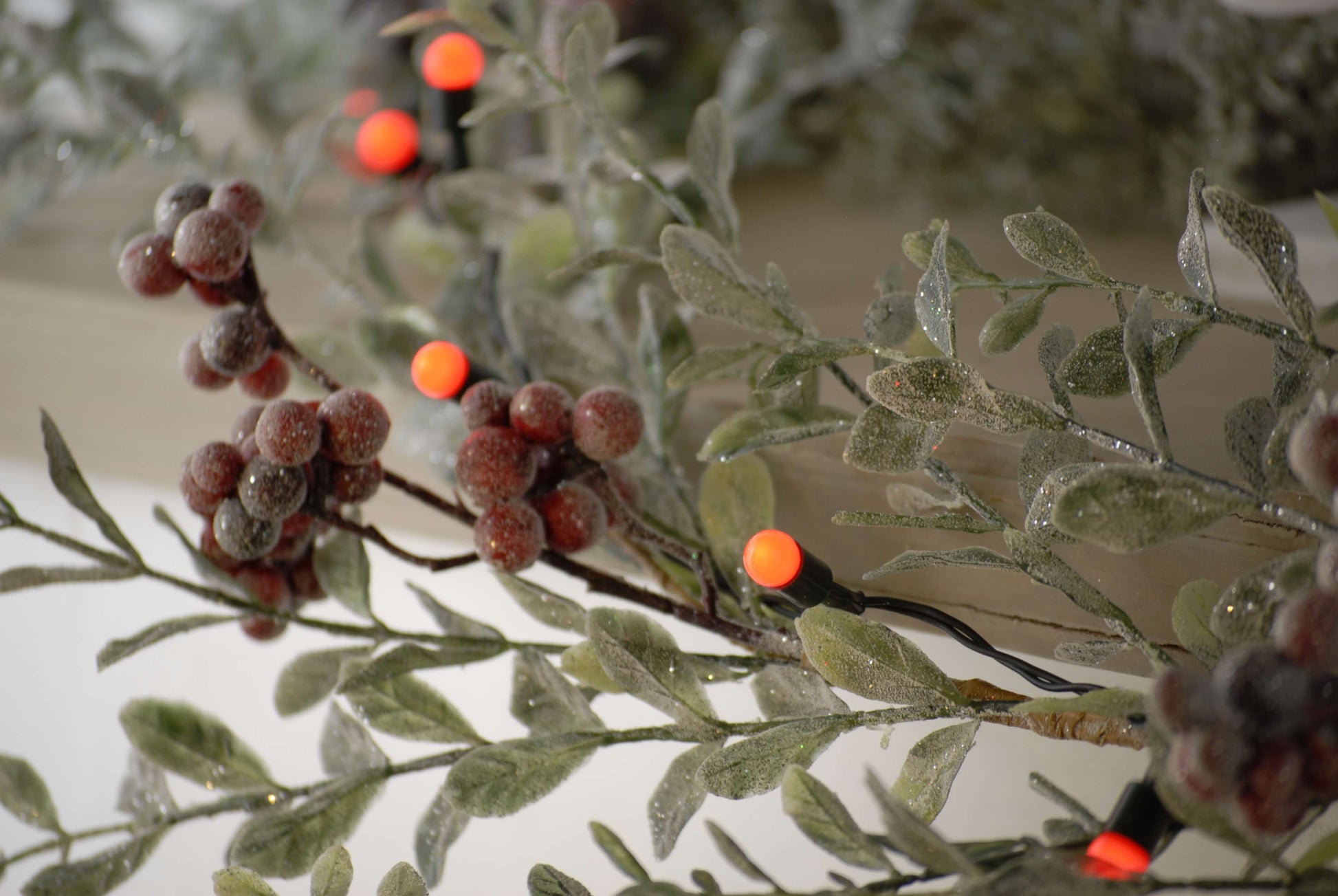 Shwoign a close up of the red berries Christmas lights bulbs next to an artificial berry stem