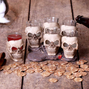 Showing the skull shaped shot glasses on display with a red liquid in one, and coins around the base, like buried treasure