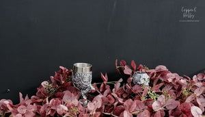 Shot against a black background, showing the skull tea light candle holder nestled in amongst a burgundy Christmas garland
